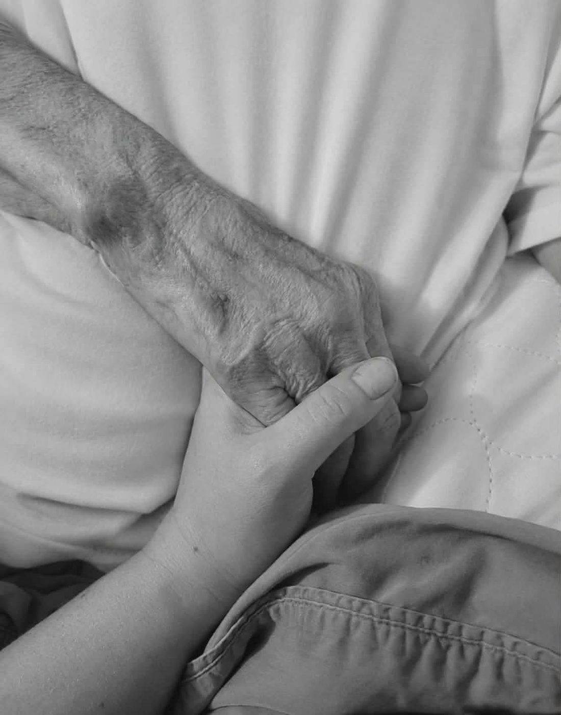 A younger hand gently holding the hand of an elderly person at rest.